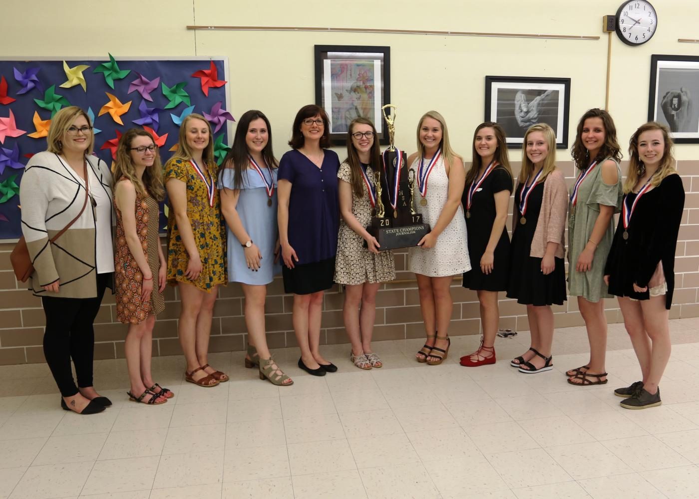 Nine members and the two advisers of the EHS journalism team stand next to the championship trophy at the District 7 School Board Meeting on May 8. From left: Ms. Mudge, Maddi Lammert, Jane Thompson, Jamie Skigen, Mrs. Thrun, Erin Morrisey, Morgan Goebel, Emma Lipe, Sophie Kraus, Jade Weber and Nara Markowitz.