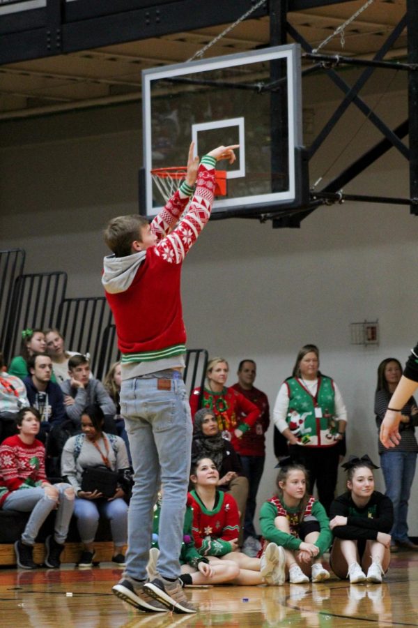 Senior Grant Schaefer shoots a basketball in a last minute shootout between two players on the varsity boys basketball team against two players on the varsity girls basketball team. Students look uninterested in the background.