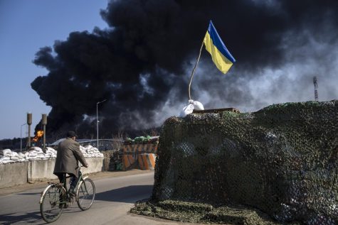 A man rides a bicycle as black smoke rises from a fuel storage of the Ukrainian army following a Russian attack, on the outskirts of Kyiv, Ukraine, Friday, March 25, 2022. 