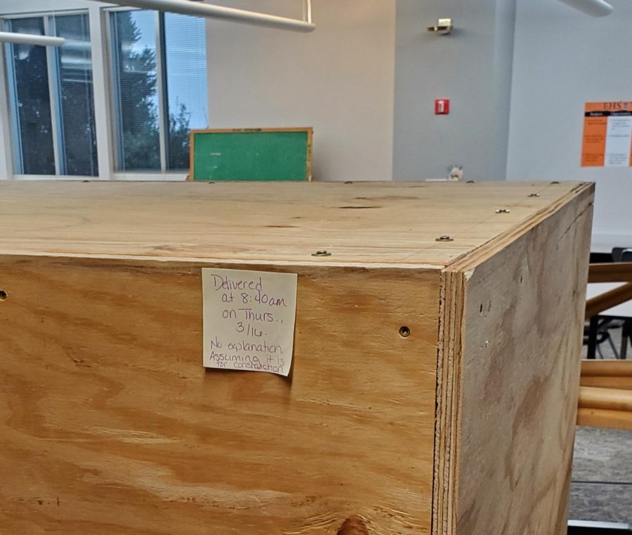 A large wooden box in the media center with a sticky note reading, "Delivered at 8:40 am on Thurs., 3/16. No explanation. Assuming it is for construction."